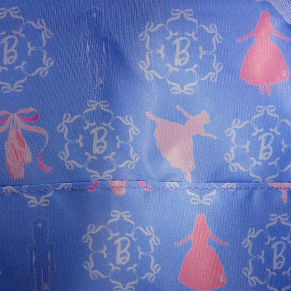 A close-up of a blue fabric surface with a repeating pattern of white ornamental motifs, ballerina silhouettes, and pink ballet shoes and dresses.