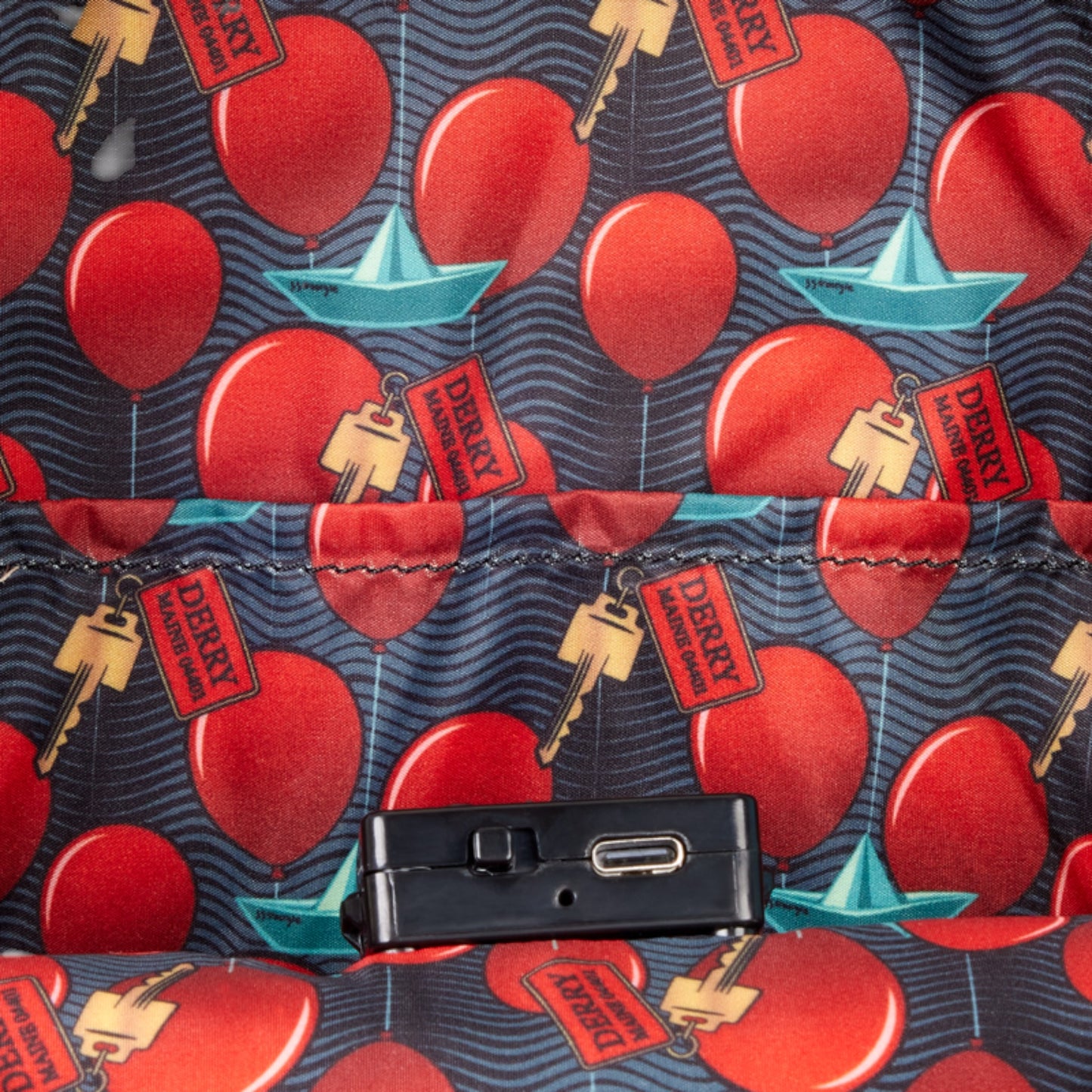 Inside of Loungefly IT Pennywise Cosplay Light-Up Mini Backpack with patterned fabric with red balloons, blue boats, and 'Derry' labels on a dark background.