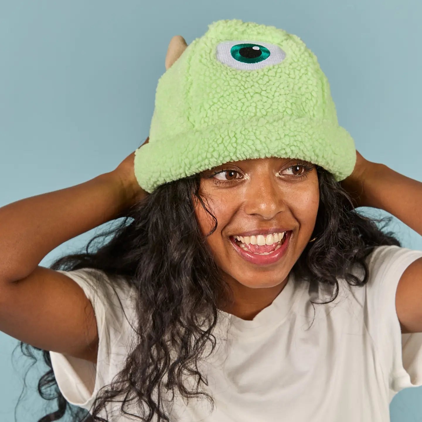 Person wearing a Mike Wazowski Sherpa Beanie with a single eye on a light blue background