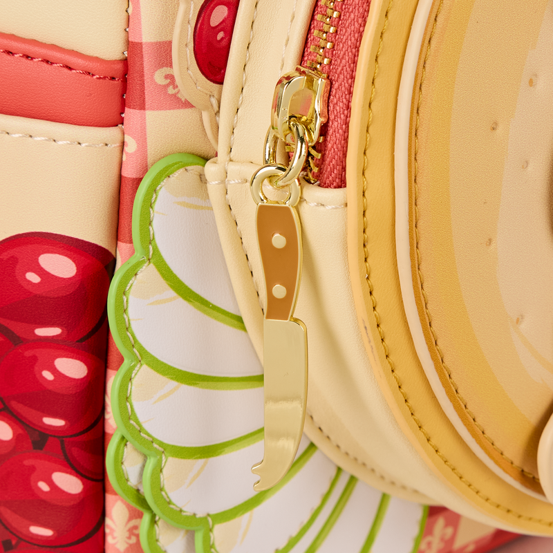 Side view close-up of the with a mini backpack showing a knife charm and cherry design.