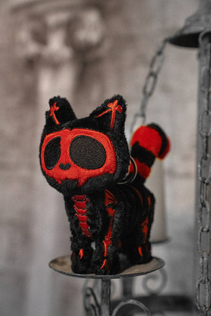 Black and red plush cat on a metal stand with a blurred background
