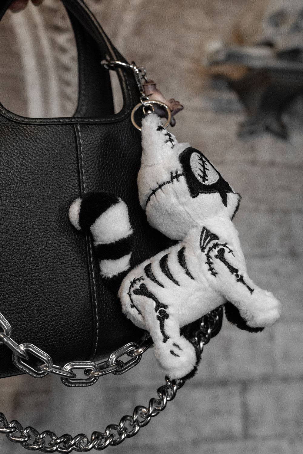 Black and white cat plush keychain attached to a black handbag with a blurred background.