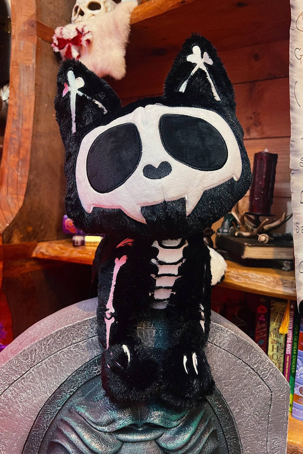 A black and white skeleton cat plush bag sitting on a gray decorative surface in a wooden shelf display.