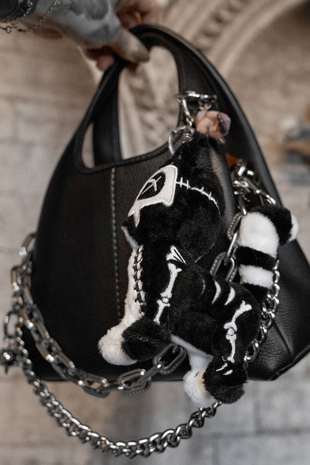 Black handbag with a cat skeleton keychain and chain detail held by a person.