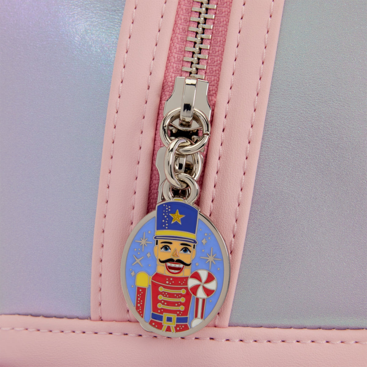 Close-up of a pastel pink and lavender bag with a silver zipper and a colorful nutcracker-themed oval zipper pull.