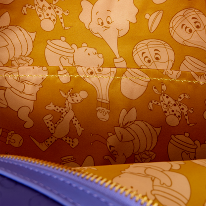 Close-up of the interior lining of a zippered pouch or bag, featuring a warm yellow-orange background with a repeating pattern of Winnie the Pooh characters including a bee, elephant, giraffe, and hot air balloon in cream outlines.