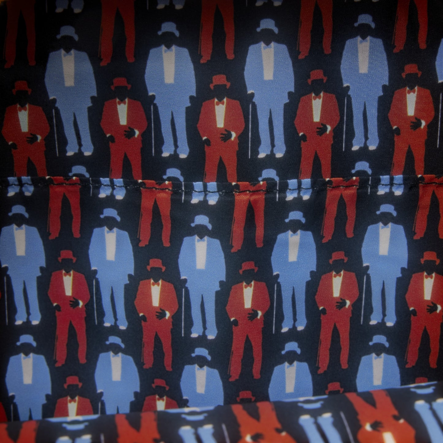 A close-up of patterned fabric featuring repeated stylized figures in red and light blue suits on a dark navy background.