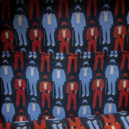 A close-up of patterned fabric featuring repeated stylized figures in red and light blue suits on a dark navy background.
