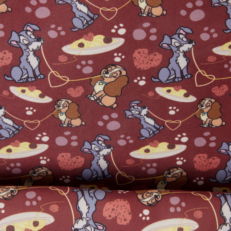 A close-up of patterned fabric featuring Lady & the Tramp with hearts, paw prints, and pizza slices on a dark red background.