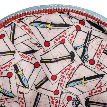 Close-up of inside of Loungefly Child's Play Chucky Cosplay Mini Backpack with a knife, hammer, scissors, and Chucky text patterned fabric design on a white background