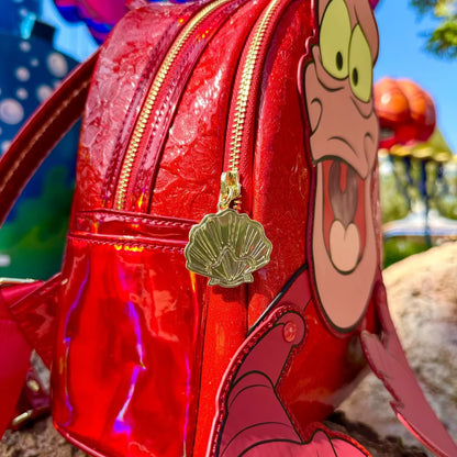 Red backpack with The Little Mermaid Sebastian Metallic character face and shell zipper charm, outdoor background