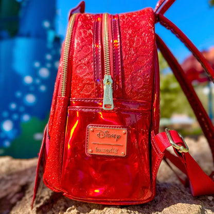 Red glittery The Little Mermaid Sebastian Metallic backpack with Disney logo on a blurred outdoor background