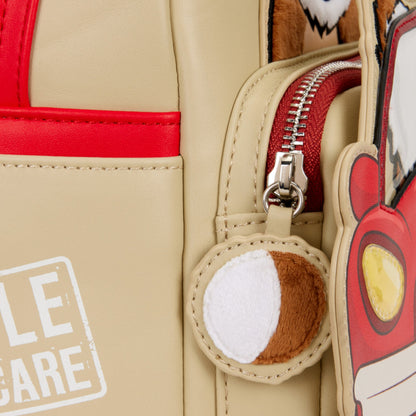 Close-up of a beige backpack with red accents, a gizmo character zipper charm, and a patch.