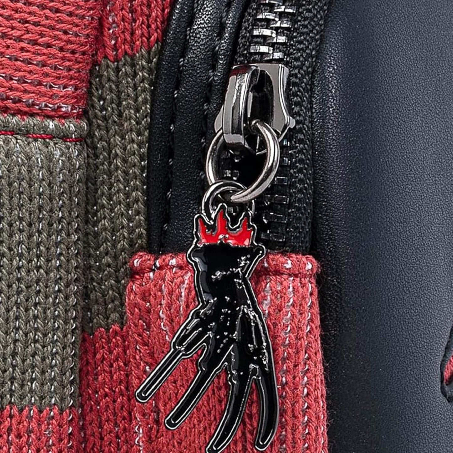 Close-up of Loungefly Nightmare On Elm Street Freddy Kreuger Sweater Mini Backpack with silver hand holding a gloves with knives for fingers zipper charm