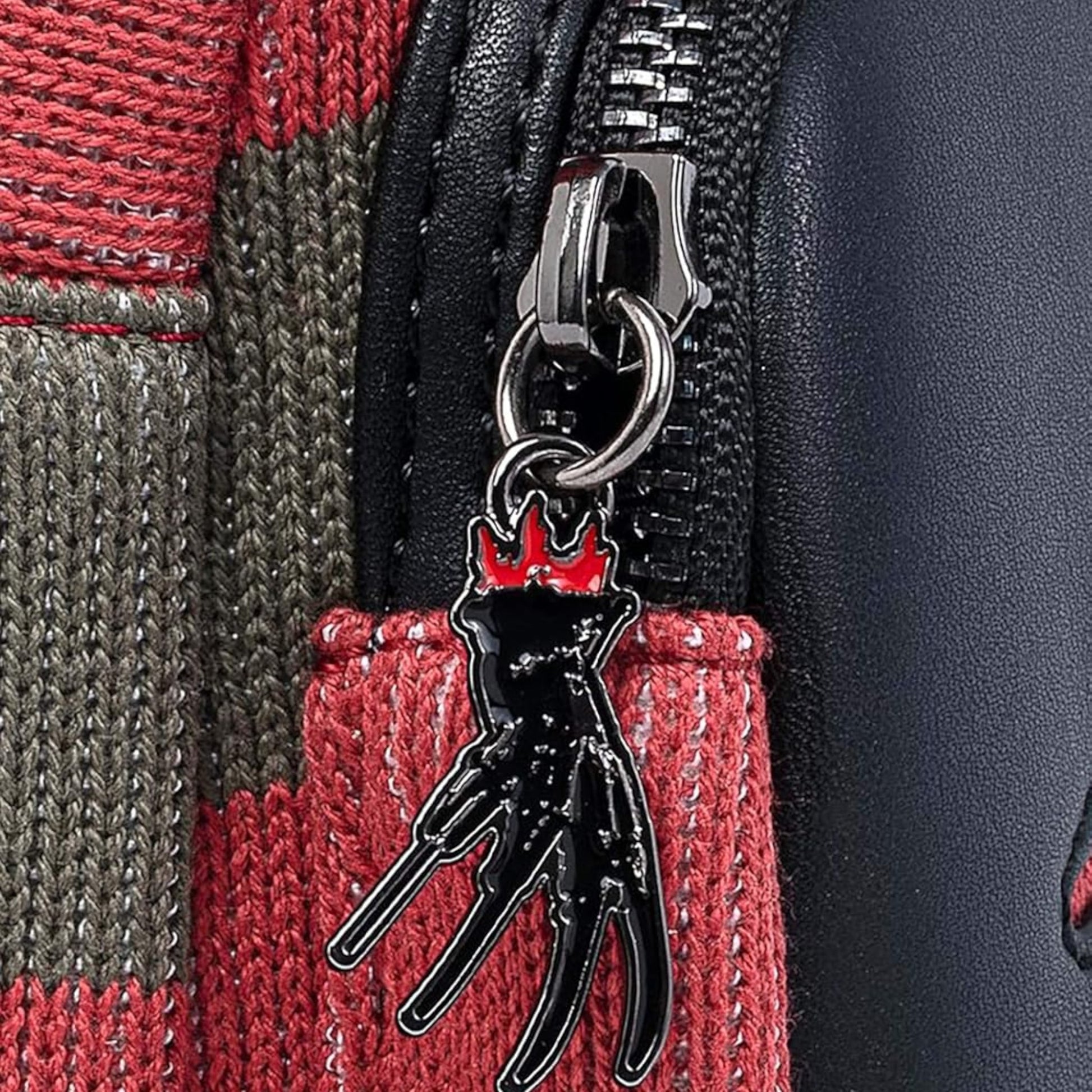 Close-up of Loungefly Nightmare On Elm Street Freddy Kreuger Sweater Mini Backpack with silver hand holding a gloves with knives for fingers zipper charm