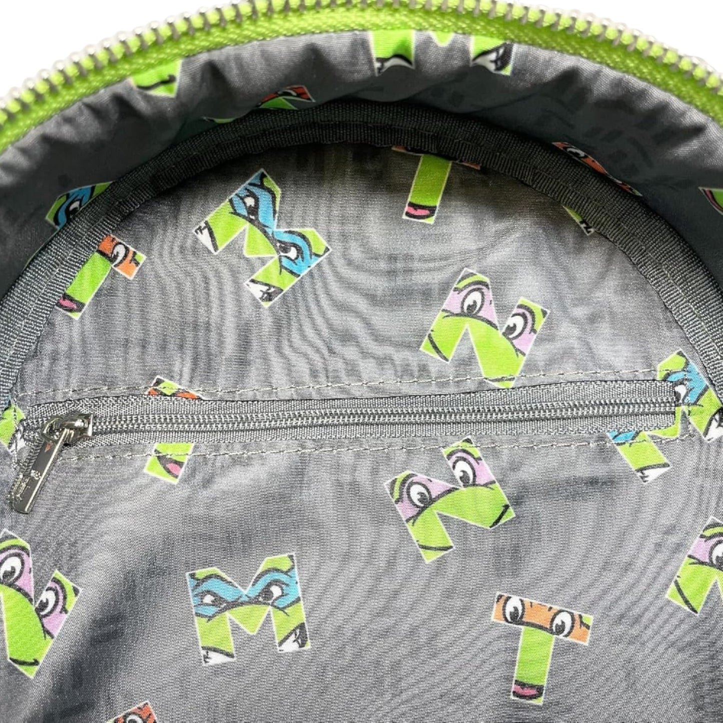 Close-up of a gray bag with colorful letter 'M' stickers on a green zipper background