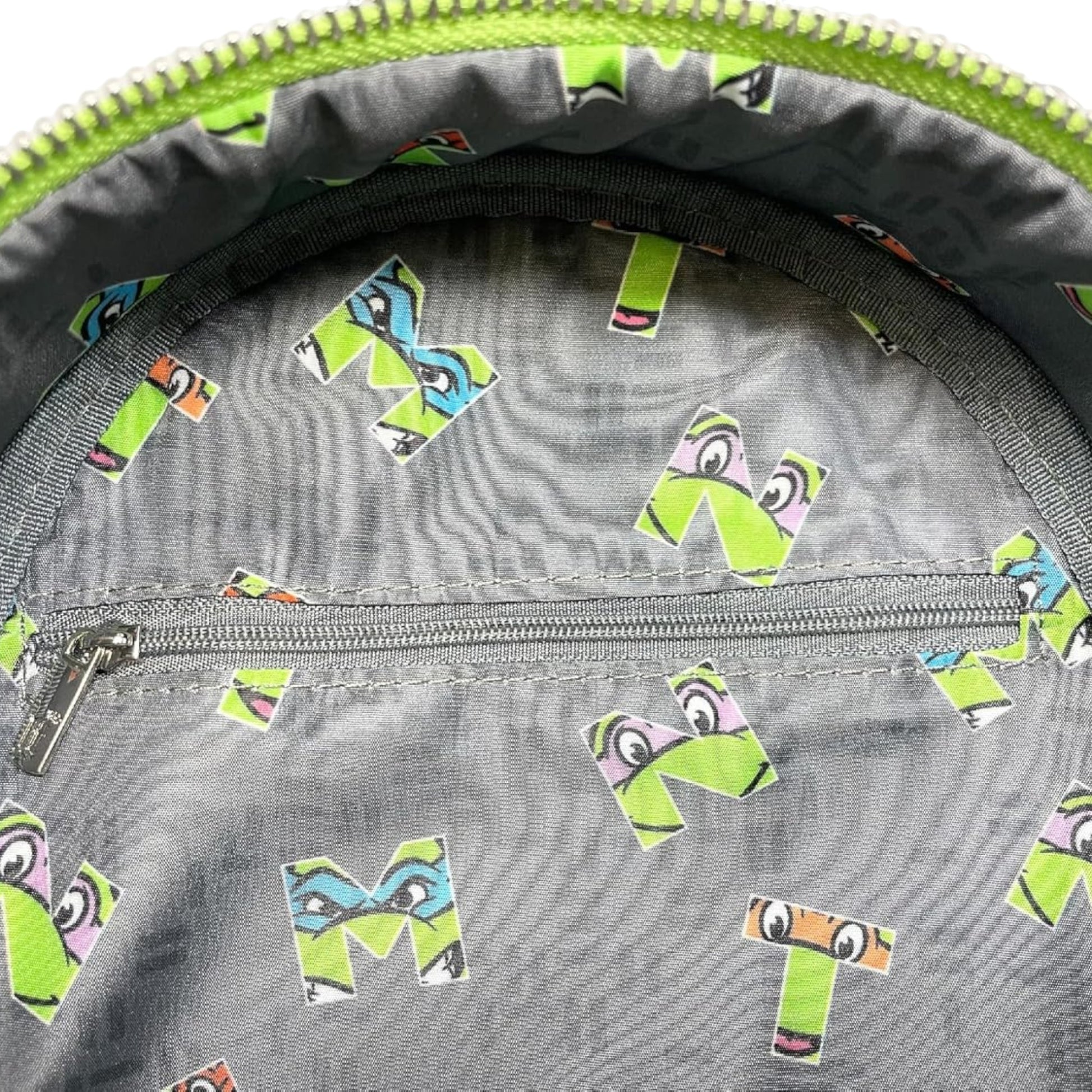 Close-up of a gray bag with colorful letter 'M' stickers on a green zipper background