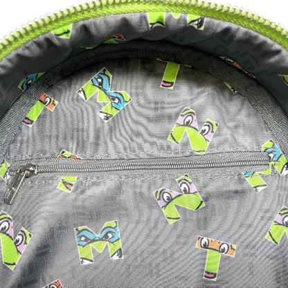 Close-up of a gray bag with colorful letter 'M' stickers on a green zipper background