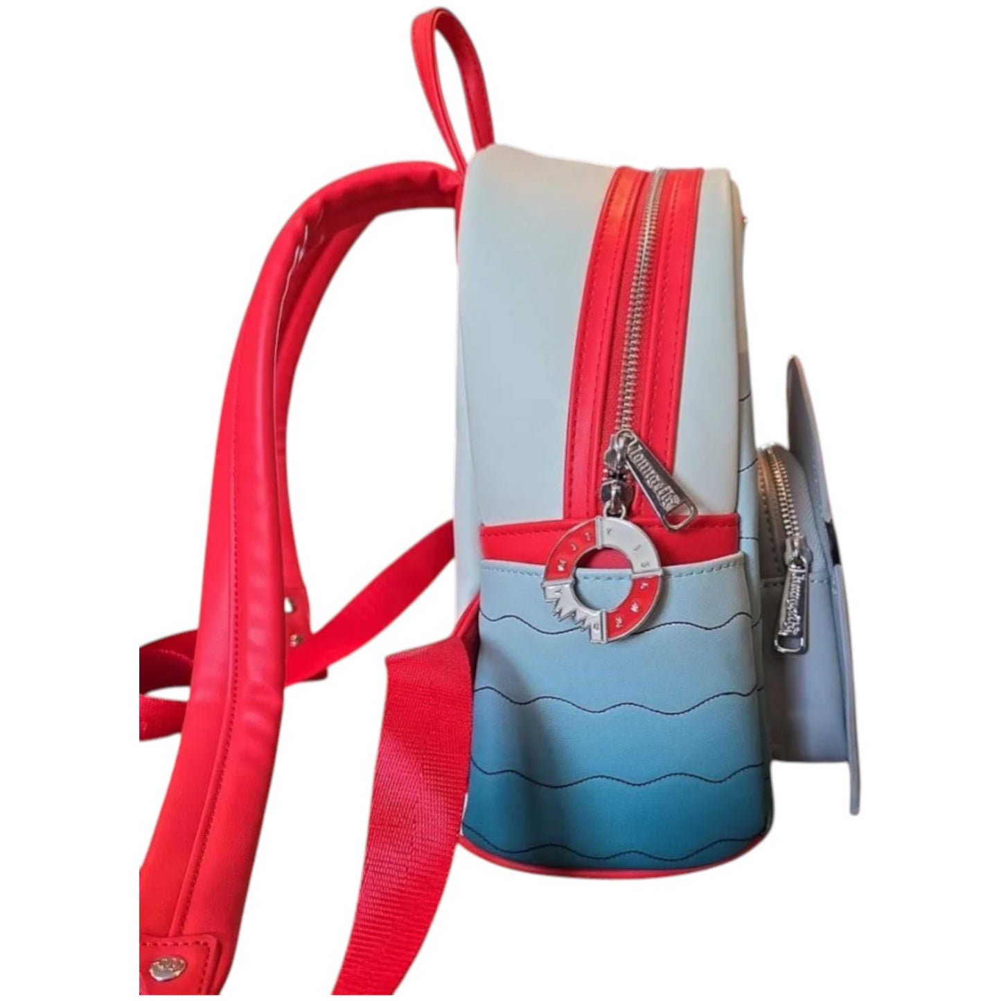 Side of Loungefly Universal Studios Jaws Mini Backpack with red and blue design and a innertube with a bite out of it zipper charm on a white background