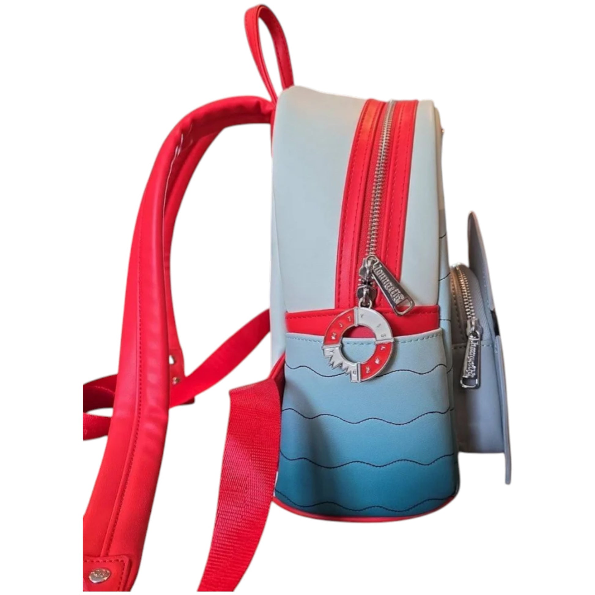 Side of Loungefly Universal Studios Jaws Mini Backpack with red and blue design and a innertube with a bite out of it zipper charm on a white background