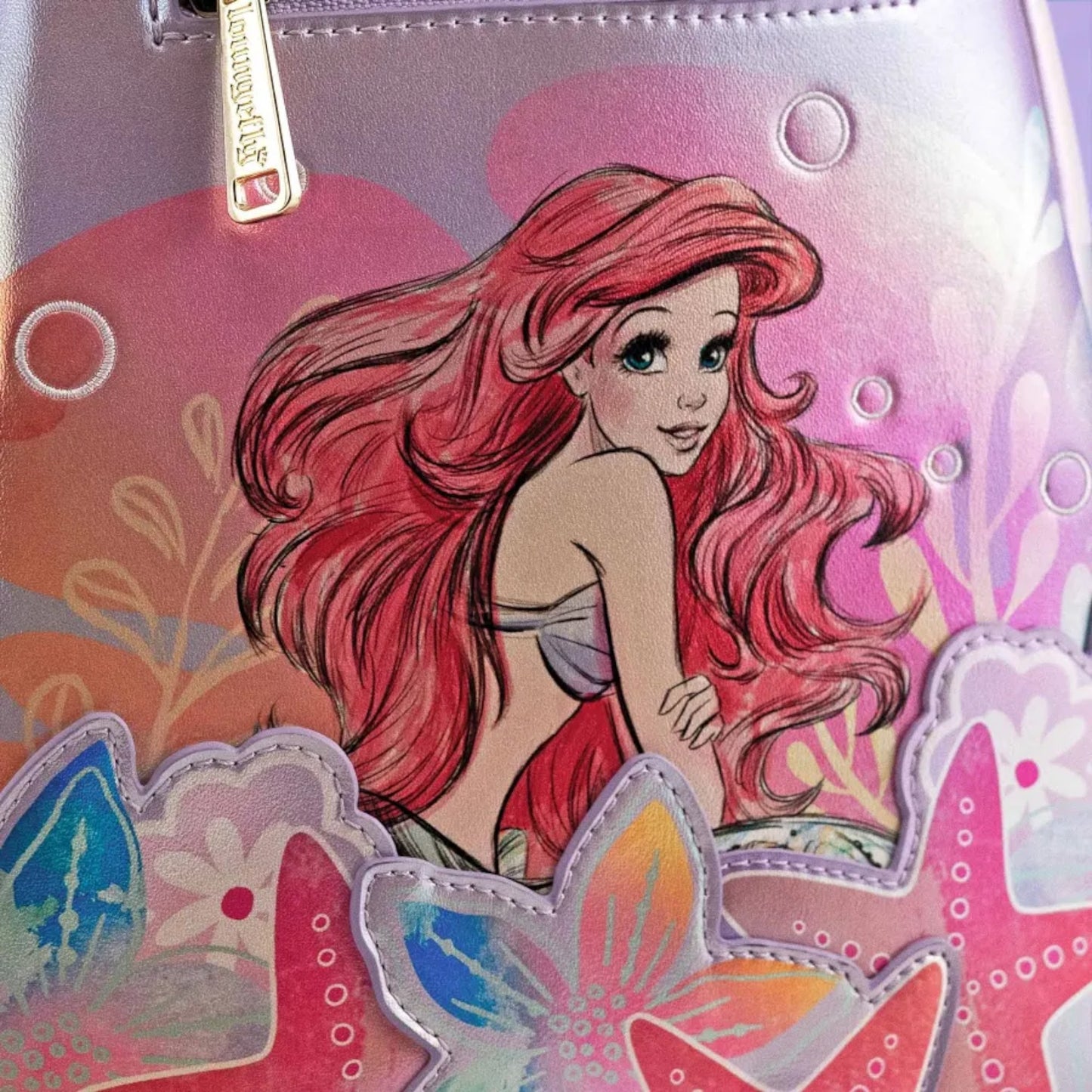 Close up of Loungefly Disney The Little Mermaid Ariel Soft Floral Mini Backpack with Ariel sitting around seashells and flowers 