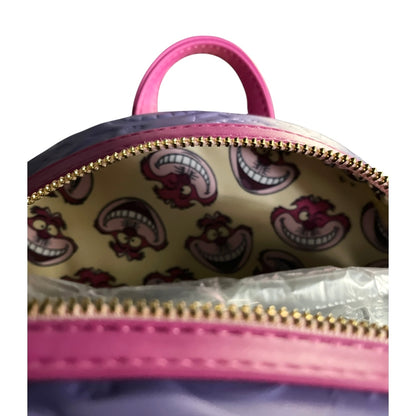 Close-up of a pink bag with a gold zipper, showing Cheshire Cat-themed patterns inside.