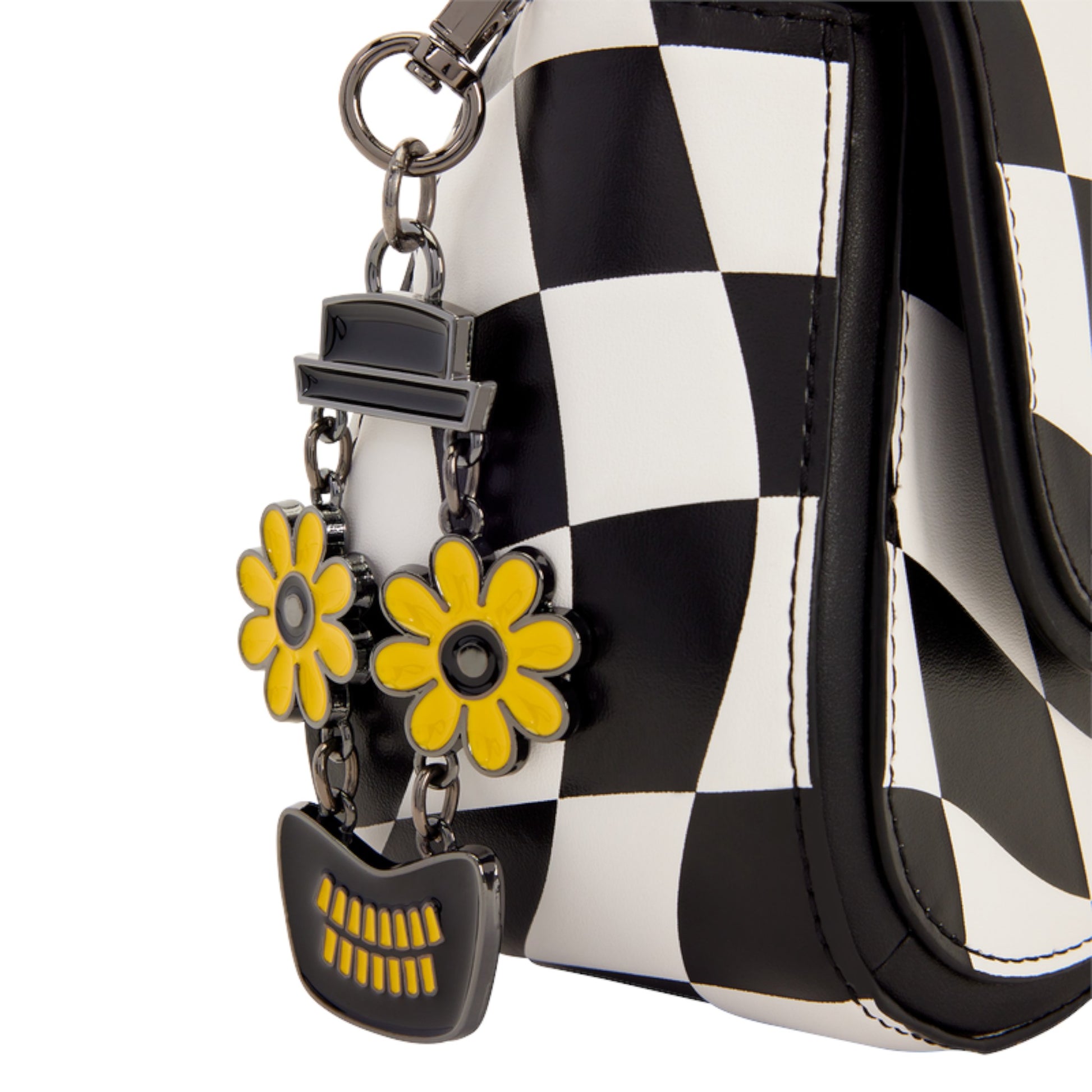 Close-up of a black and white checkered handbag with a black leather strap and a hanging charm featuring two yellow flower charms and a black mouth-shaped accessory.