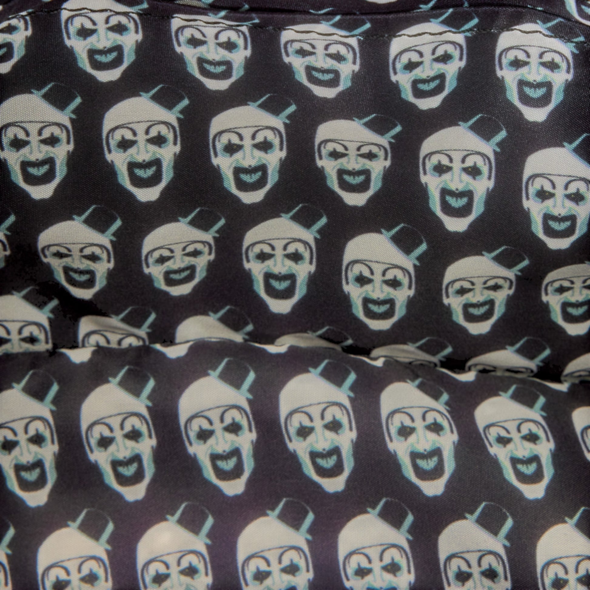 Close-up of a fabric surface with a repeating print of stylized clown faces in white and pale blue on a very dark charcoal background.