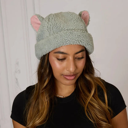 Woman wearing a grey The Aristocats Berloiz Sherpa beanie with pink ears against a white background