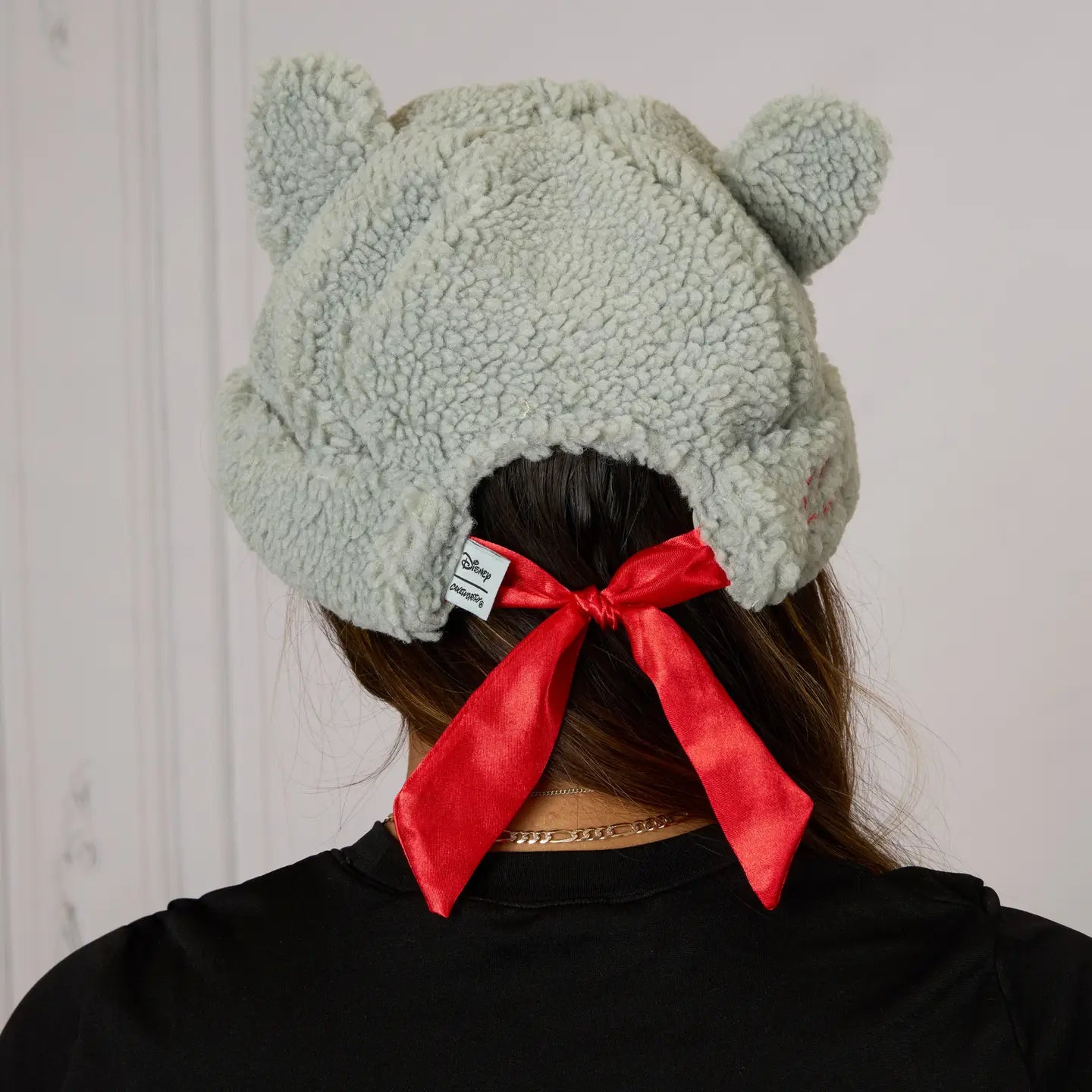 Person wearing a The Aristocats Berloiz Sherpa Beanie with animal ears and a red bow, against a white background.