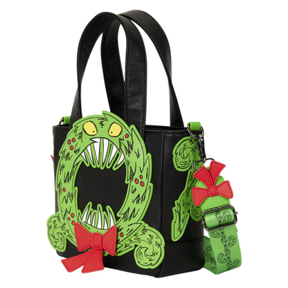 A black faux-leather tote bag featuring a large green monster face wreath design on the front, with red bows and a matching green patterned strap hanging from the side.