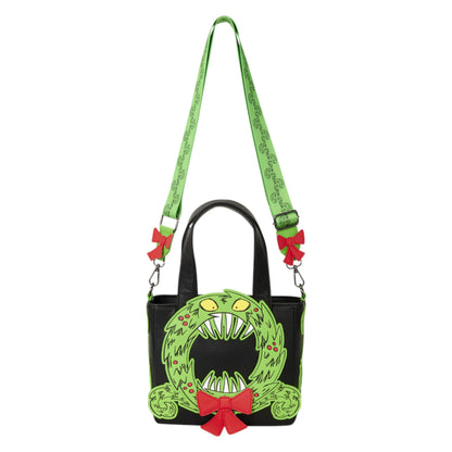 A black handbag with a green monster face design on the front, a green patterned shoulder strap, and red bow accents, shown on a plain white background.