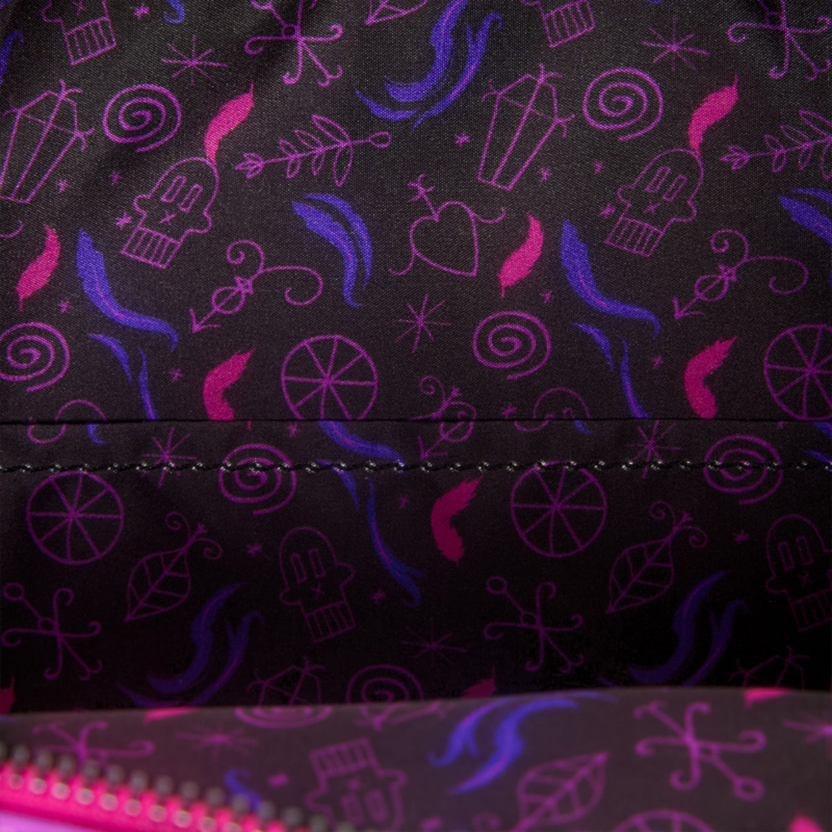 Close-up of a black fabric surface with an allover repeating pattern of pink and purple whimsical doodles, including hearts, stars, swirls, and abstract shapes. A stitched seam runs horizontally across the center.