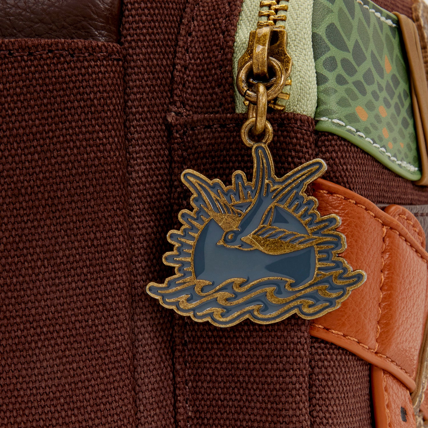 Close-up of Loungefly Pirates of the Caribbean Jack Sparrow Cosplay Mini Backpack with decorative pirate symbol zipper charm on a brown textured surface.