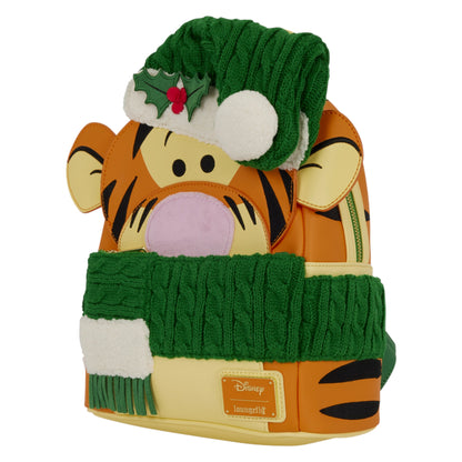 A Disney Tigger backpack styled with a winter holiday theme, featuring a green knit Santa hat with a holly accent and a matching green and white knit scarf, on a plain white background.