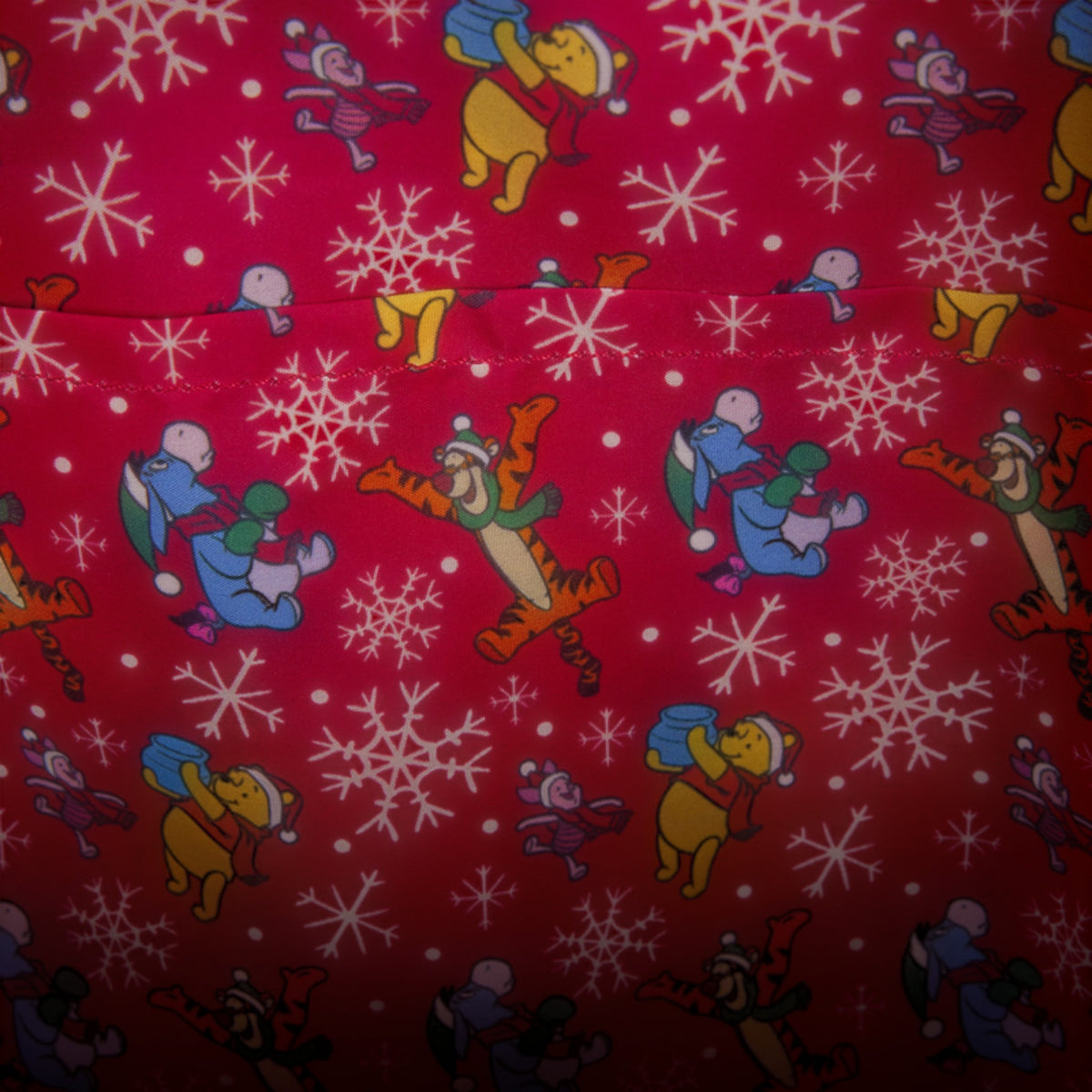 Red fabric with a repeating pattern of Winnie the Pooh characters like Tigger, Piglet, and Eeyore carrying blue snowballs, alongside white snowflakes.