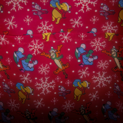 Red fabric with a repeating pattern of Winnie the Pooh characters like Tigger, Piglet, and Eeyore carrying blue snowballs, alongside white snowflakes.