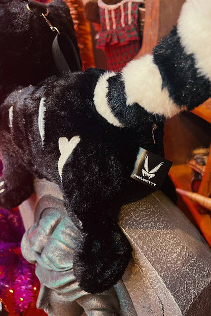 A black and white striped plush crossbody with a small black tag featuring a white logo that reads 'VampireFreaks', resting on a metallic surface in a shop setting.