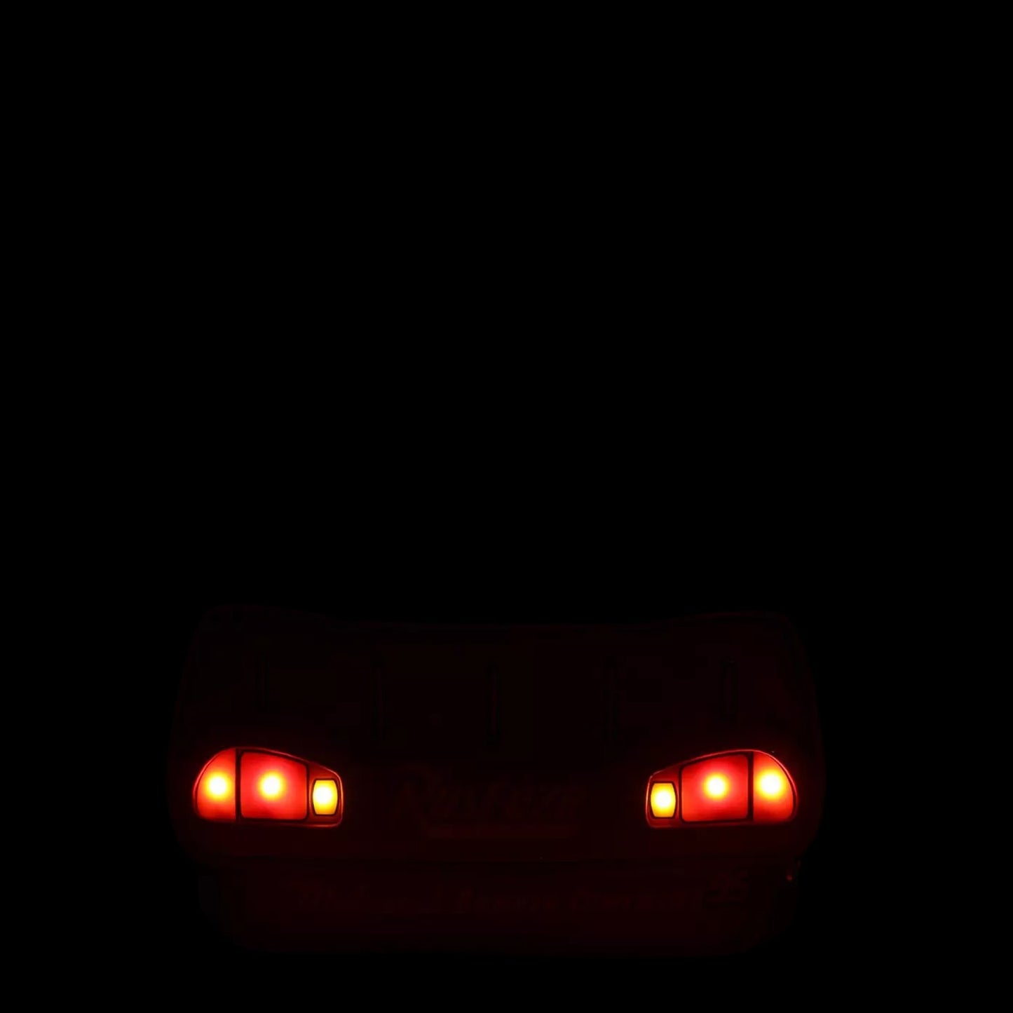 Two red headlights glowing on a dark background