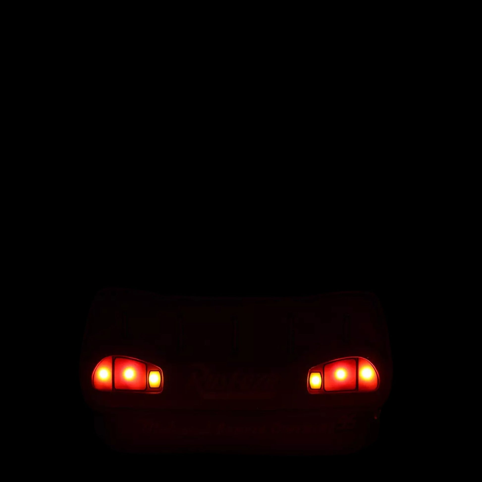 Two red headlights glowing on a dark background