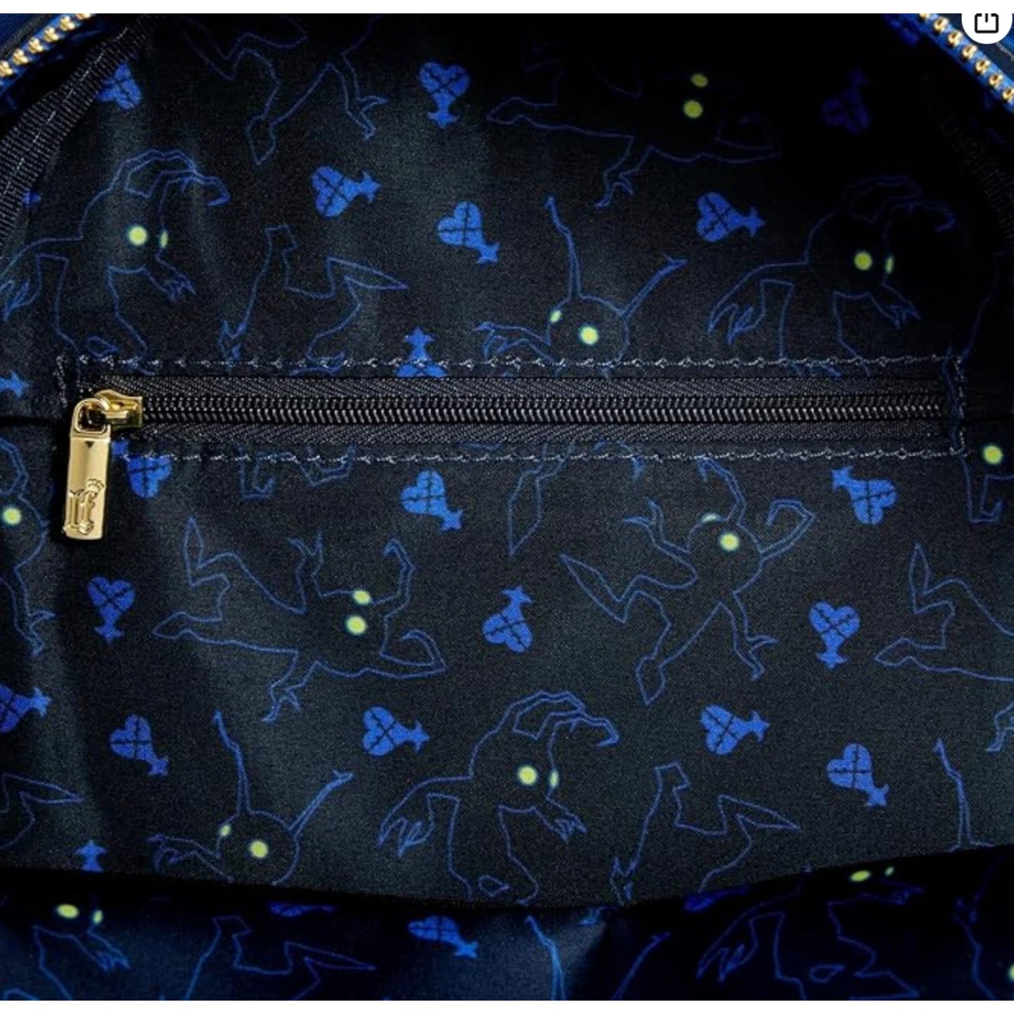 Black inside lining of mini backpack with blue ghost patterns and a gold zipper on a dark background