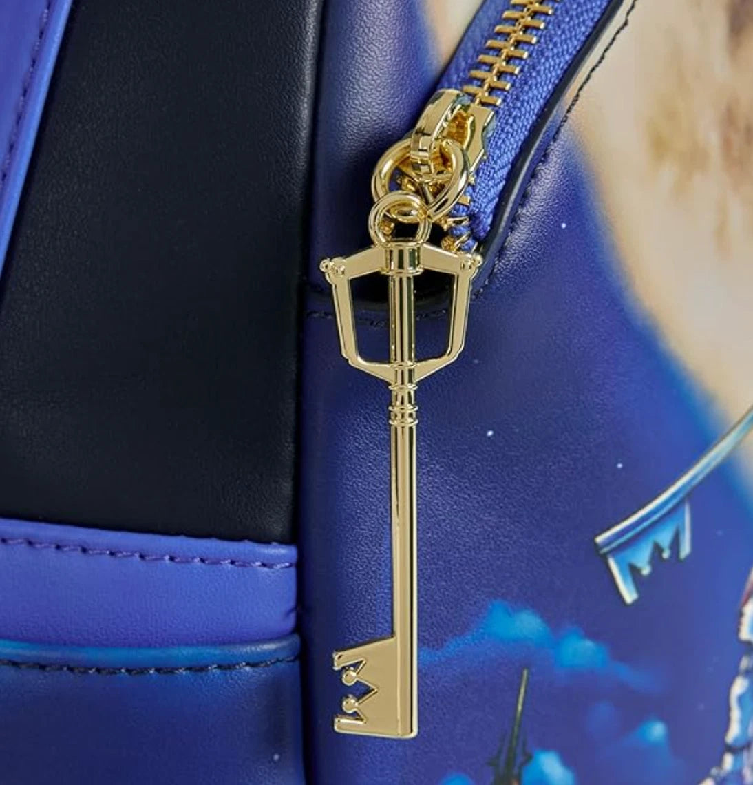 Gold key-shaped zipper charm on a blue bag with a castle design.